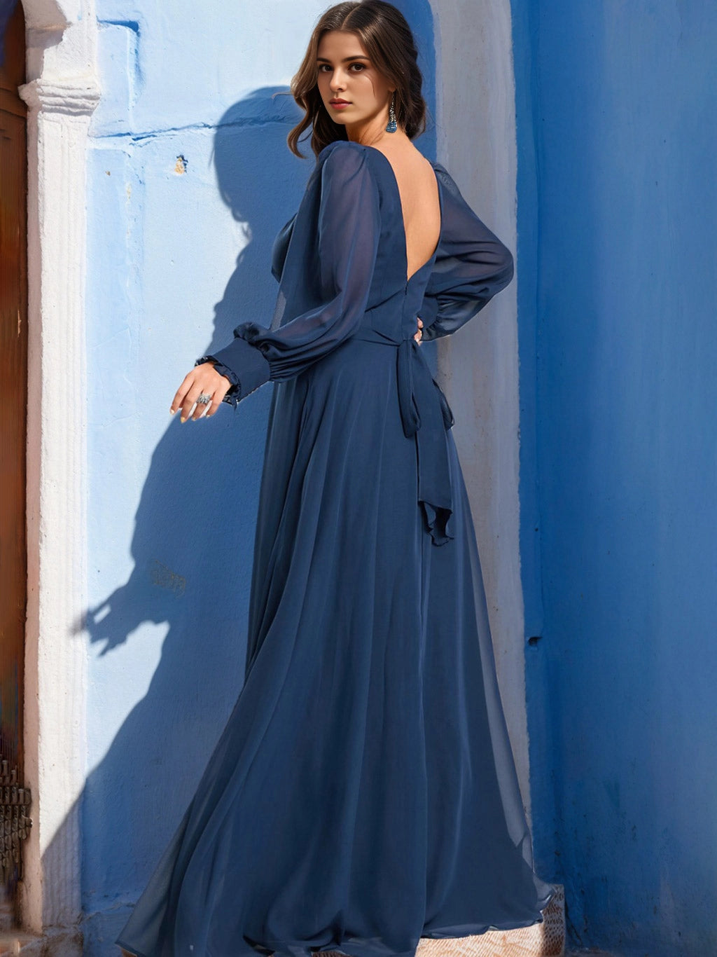 Back view of RoselleDress dark blue curvy evening dress deep open v back self tie bow cuffed long sleeve flowy chiffon maxi gown