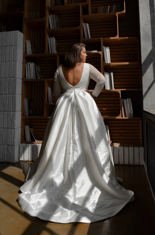 White plus size long sleeve wedding dress featuring deep V-back, center zipper, shimmering bodice and full satin-look ball gown skirt with train