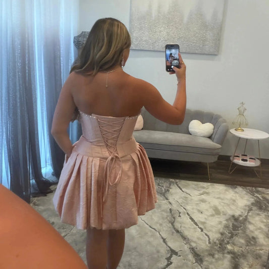 Plus size blush pink homecoming dress featuring crisscross lace-up corset back and pleated skirt
