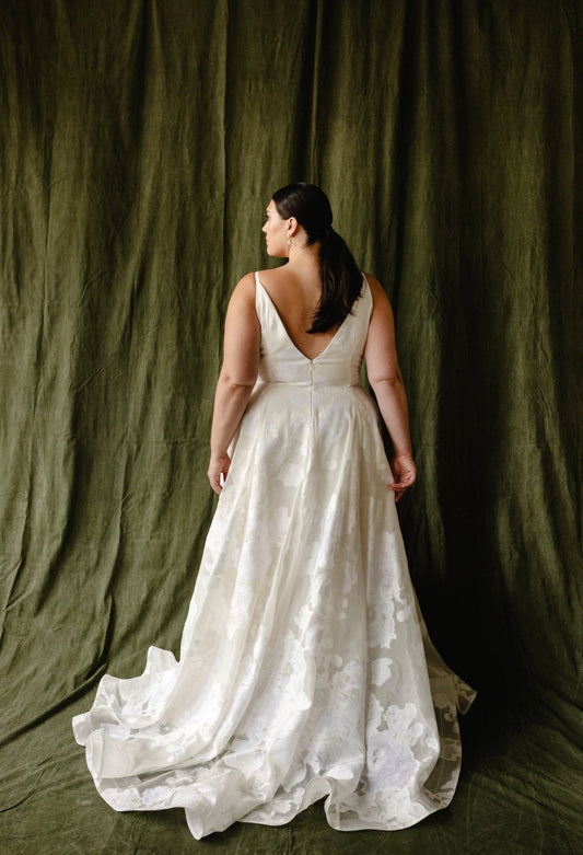 Ivory plus size floral wedding dress featuring deep V-back, center zipper closure, fitted waist and flowing A-line skirt with sweep train