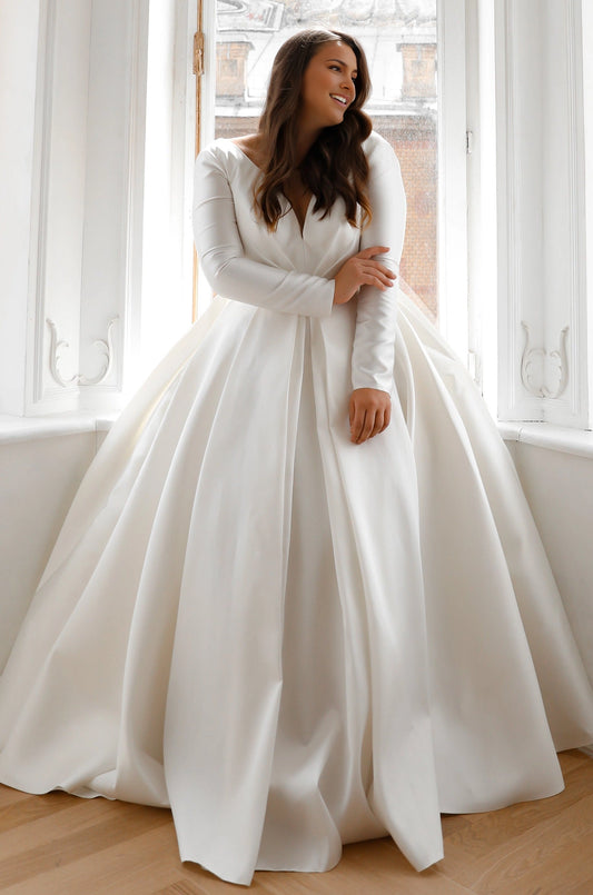 Ivory plus size ball gown wedding dress with plunging V-neckline, elegant long sleeves, fitted waist and voluminous floor-length skirt