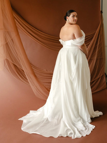 Ivory plus size wedding dress with draped off-shoulder sleeves, button-detail back, defined waist and flowing chiffon-look skirt with sweep train