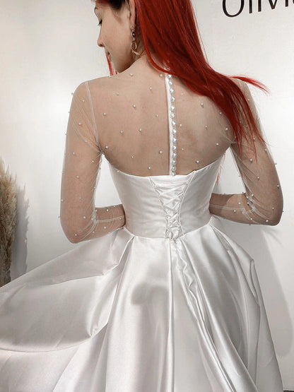 White satin-look wedding dress with lace-up corset back, pearl embellished sheer long sleeves and pleated bridal skirt